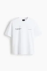 Remera de punto de algodón color blanco, con cuello redondo ribeteado, hombros caídos y manga corta. Presenta un pequeño diseño estampado en el pecho con texto en tipografía cursiva.