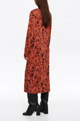 Vestido midi de corte fluido con escote redondo y detalle fruncido en el centro del pecho. Presenta mangas largas y un estampado abstracto en tonos rojizos y negros.