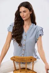 Camisa de lino y viscosa color beige, con cuello mao, escote en V y botones frontales de madera. Presenta mangas cortas con volados delicados.