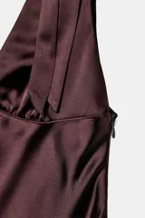 Vestido midi satinado color marrón, con escote en V y tirantes anchos ajustables con lazada en los hombros. Presenta cierre lateral con cremallera oculta.