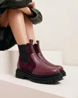 Bota tipo chelsea de caña media, confeccionada en una combinación de cuero vacuno texturizado y gamuza en tono bordó. Presenta paneles laterales elásticos en color negro, suela track de goma negra con plataforma y tiradores en la parte superior para facilitar el calce.