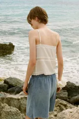 Top blanco de escote recto y tirantes finos ajustables, con detalle de lazos a contraste y flores bordadas. Cierre frontal con botones forrados en el mismo tejido.