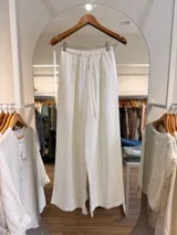 Pantalón blanco de calce amplio y relajado, confeccionado en mezcla de lyocell y lino. Presenta cintura elástica con cordón de ajuste, bragueta falsa con botones decorativos y bolsillos laterales.