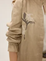 Camisa de lino color crudo, con cuello mao y cierre frontal con botones. Cuenta con detalles de alforzas verticales y diseño bordado floral en el frente, además de mangas 3/4 con volumen y puños elásticos.