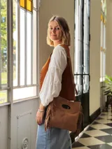 Cartera bandolera de cuero color camel, con forro interno de tela y flecos laterales.