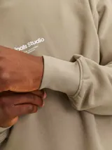 Buzo de cuello redondo y manga larga, corte relajado en color beige. Presenta el logotipo "Originals Studio" estampado en pequeño en el pecho.