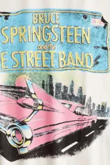 Remera color crema de corte oversized, con estampado de una patente con el nombre de Bruce Springsteen y un auto clásico rosa. Cuello redondo ribeteado.