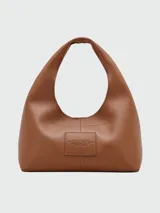 Cartera tipo hobo Marc Jacobs modelo The Sack, confeccionada en cuero granulado color marrón. Presenta un diseño minimalista con el nombre de la marca y el modelo estampados en el frente y una correa integrada al cuerpo de la cartera.