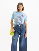 Remera celeste de jersey de algodón pima, con mangas cortas, escote redondo y silueta relajada. Cuenta con estampa frontal en serigrafía con relieve de Buda con elementos de la Estatua de la Libertad.