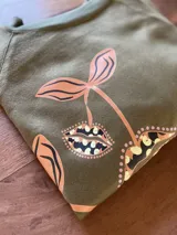 Buzo cropped de algodón color verde militar, con mangas ranglan y diseño estampado en el frente con motivos de besos y moños. Cuenta con elástico holgado en la cintura y los puños.