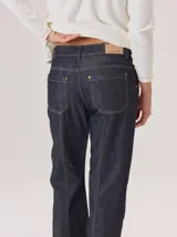 Jean de corte recto confeccionado en denim azul oscuro, con costuras a la vista en color rojo contrastante. Presenta un diseño de tiro alto con bolsillos frontales y cierre de botón.