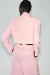 Blazer corto rosado con cuello solapa, hombreras y mangas largas. Cuenta con cierre cruzado delantero con dos botones oscuros y un bolsillo de ojal en el pecho.
