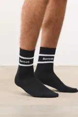Medias altas de algodón color negro, con diseño acanalado y dos franjas blancas horizontales en la parte superior que enmarcan el logo de la marca Basset en tipografía gótica.