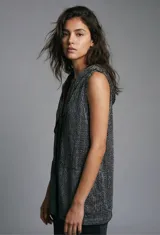 Chaleco de punto calado color beige, sin mangas, con capucha y bolsillos delanteros.