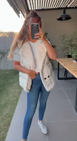 Chaleco puffer blanco con cuello de piel sintética y cierre con broches metálicos.