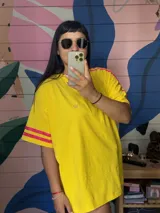 Remerón oversize amarillo con cuello redondo y mangas cortas con detalle de dos cintas de terciopelo fucsia en los hombros.
