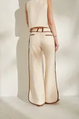 Pantalon de lino color beige claro con detalles de ribetes en tono marron oscuro en los bolsillos, trabillas y laterales de las piernas. Presenta corte recto y amplio con tiro medio.
