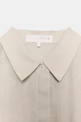 Camisa de lino 100% color beige claro, de manga larga y cuello solapa, con cierre frontal de botones.
