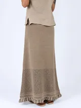 Pollera larga de punto color marrón, con diseño calado en el dobladillo y detalles de volados y costuras en tono rojizo.