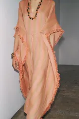 Vestido largo tipo kaftán confeccionado en lino a rayas verticales en tonos naranja y verde. Tiene cuello redondo con escote en V, mangas cortas amplias, acabado deshilachado y cinturón de cordón en el mismo tejido.