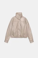 Chaqueta color beige de efecto piel, con cuello subido, manga larga con puño y bolsillos laterales. Tiene forro interior y bajo elástico. Cierre frontal con cremallera y botones a presión ocultos por solapa.