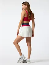 Skort deportivo blanco con pretina ancha tejida en colores fucsia y azul. Cuenta con short incorporado en el interior y diseño plisado central, inspirado en el estilo de tenis vintage.