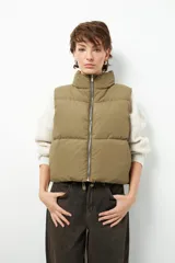 Chaleco puffer color beige, sin mangas, con cuello alto y cierre frontal con cremallera.