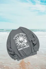 Buzo gris con estampado de sol, palmeras y olas en la espalda, con texto "Glassy Waves Surf Co. Sunset Chasers".