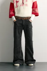Jeans flare fit de denim de algodón negro con efecto desgastado, roturas, costuras decorativas en las perneras y bajo irregular deshilachado.