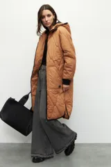 Campera de nylon larga oversized color negro, con capucha, tres bolsillos externos y uno interno. De tela capitoneada, con puños en las mangas y forro polar.