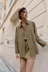 Chaqueta de corte recto y estilo camisero en color beige, con cuello solapa, manga larga y cierre frontal con botones. Presenta dos bolsillos delanteros de plastrón.