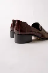 Mocasín de cuero con textura de reptil en color bordó, con puntera cuadrada y taco bloque bajo de color negro.