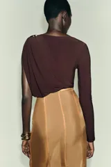 Body de manga larga color marrón oscuro, con escote asimétrico drapeado y detalle de broche metálico en el hombro derecho.