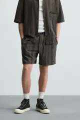 Bermuda de algodón color blanco, de corte relajado (relaxed fit), con cintura elástica ajustable mediante cordón. Posee bolsillos laterales y un bolsillo trasero de plastrón. Presenta un bordado en contraste en la pernera.