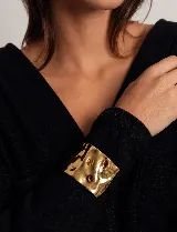 Brazalete rígido de acero quirúrgico con acabado dorado brillante y superficie texturizada con efecto irregular.