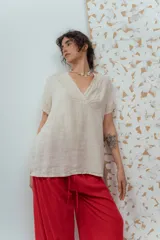Blusa de lino color beige de calce relajado, con escote en V y detalles de pliegues frontales. Posee mangas cortas y una silueta suelta.