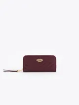 Maxi billetera de cuero vacuno con diseño matelassé en forma de V. Presenta un aplique metálico dorado en forma de labios en el frente y cierre perimetral con tirador de cuero.