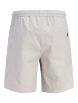 Bermuda de calce relajado color beige, con cintura elástica con cordón de ajuste, bolsillos delanteros y traseros, confeccionada en tejido dobby con textura sutil y un toque de elasticidad.
