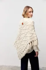 Poncho de tejido de punto grueso color crudo con diseño de trenzas, cuello alto y terminación con flecos en el ruedo.