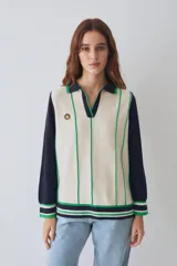 Remera tejida de algodón estilo polo con mangas largas en color azul marino y cuerpo en color beige con líneas verticales verdes. Presenta cuello polo, puños y ruedo con franjas decorativas y un pequeño parche circular en el pecho.