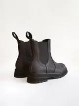 Bota tipo Chelsea de caña media, confeccionada en cuero negro con acabado mate. Presenta paneles elásticos laterales, tiradores traseros y suela track robusta con plataforma dentada.