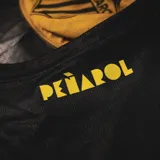 Musculosa deportiva Puma del equipo de básquet de Pefarol, modelo Away 2025. Disefo en color negro con detalles en amarillo, presenta el escudo del club en el pecho, el logotipo de Puma y una hilera de estrellas amarillas alineadas en diagonal en la parte inferior.
