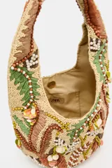 Bolso de hombro con diseño estructurado, decorado con intrincados bordados de abalorios, cuentas y apliques en tonos tierra, verde y crema. Presenta un asa integrada y cierre mediante botón imantado.