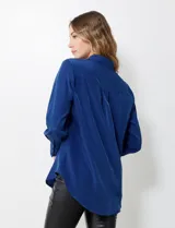 Camisa de satén color violeta, con cuello clásico, cierre frontal con botones, manga larga con puños anchos abotonados y bolsillo aplicado en el pecho.