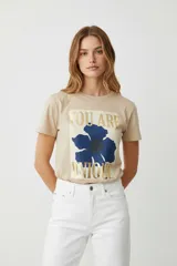Remera de algodón color beige, manga corta y cuello redondo, con estampado frontal de una flor azul y texto en foil dorado que dice "You are Unique".