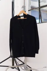 Cárdigan negro de punto liviano con cuello en V, cierre frontal con botones, bolsillos delanteros y detalle bordado.