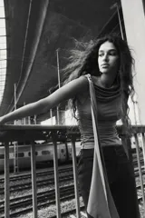 Top color marrón de punto elástico, con un hombro descubierto y una tira larga que cae desde el hombro. Presenta fruncidos en los laterales para un efecto drapeado.