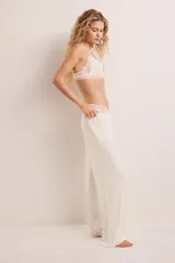 Pantalón de pijama color crema en punto pointelle, con piernas levemente acampanadas. Tiene cintura elástica revestida, ribete de volados y cordón fino para ajustar.