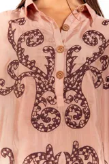 Vestido corto de silueta amplia, color tostado con bordados barrocos en contraste, escote en V con botones de madera, mangas anchas tipo capa con flecos de cuentas en los bordes.