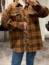 Camisa tipo sobrecamisa de corte oversize, confeccionada en tela a cuadros en tonos marrones y negros. Presenta cierre frontal con botones metálicos a presión, bolsillos frontales con solapa y mangas largas con puños abotonados.